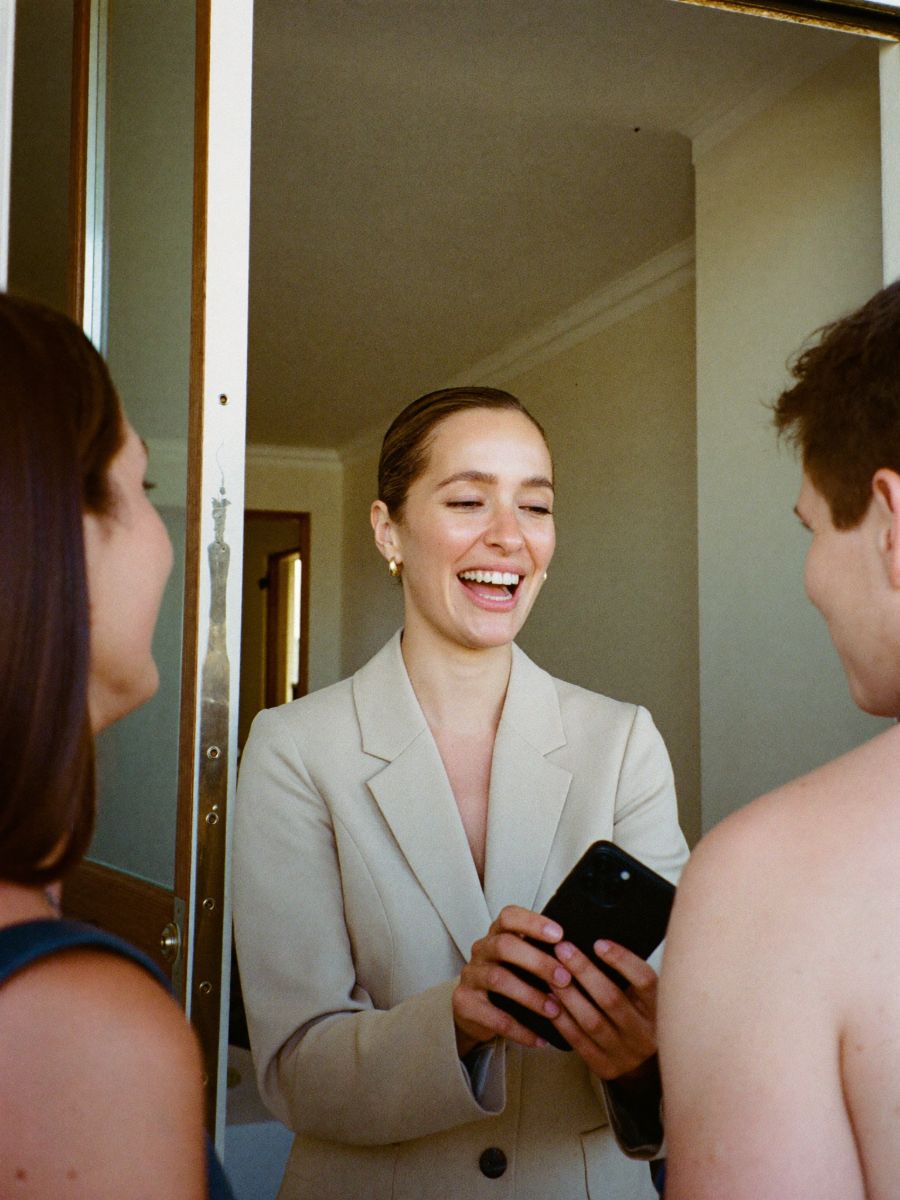 A real estate agent smiling at an apartment door, holding out her phone to a prospective client
