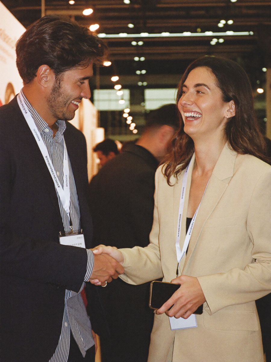 Two professionals shaking hands at a trade expo, one holding her phone